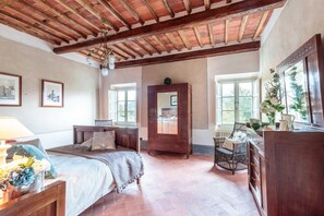Une chambre à coucher avec un lit en bois, une commode, un miroir et une fenêtre donnant sur un paysage verdoyant.