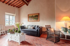 Un salon chaleureux avec un canapé gris foncé, une table d’appoint en osier, un fauteuil en osier, une armoire blanche et un tableau accroché au mur.