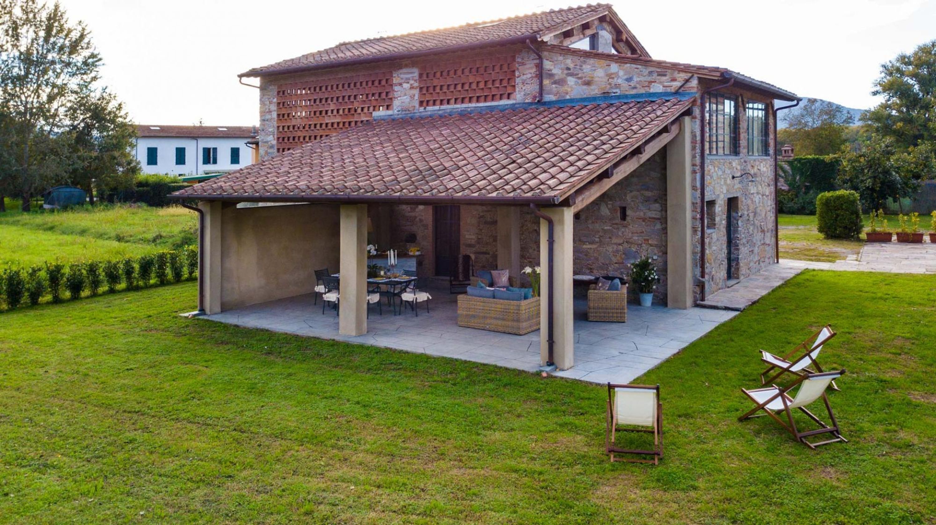 Een huis met een overdekt terras, stenen muren en een gazon.