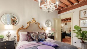 A bedroom with a wooden headboard, a large bed with multiple pillows, a nightstand with a lamp, and a chandelier. - Casa Kathy in Lucca With 2 Bedrooms and 1 Bathrooms (Lucca)