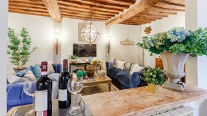 A cozy living room with a wooden ceiling, a blue sofa, a coffee table with wine bottles, and a large vase with green plants. - Casa Kathy in Lucca With 2 Bedrooms and 1 Bathrooms (Lucca)