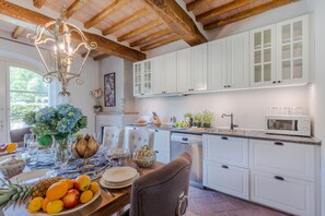 A kitchen with white cabinets, a wooden ceiling, and a dining area with a table set for a meal. - Villa Hilary in Lucca (Lucca)