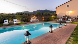 A swimming pool with lounge chairs and lanterns, surrounded by a stone wall and a building with a balcony. - Fattoria Camigliano Wine Estate (Capannori)