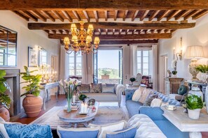 A spacious living room with a high wooden ceiling, a large chandelier, and a comfortable seating area with sofas and a coffee table. - Fattoria Camigliano Wine Estate (Capannori)