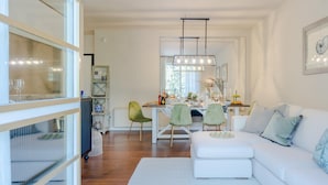 Een moderne woonkamer met een witte bank, groene stoelen en een eethoek met een witte tafel en stoelen.