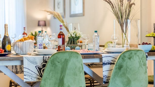 Een eetgedeelte met een moderne kroonluchter, groene bekleden stoelen en een houten tafel gedekt voor een maaltijd.