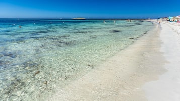 A beach with clear shallow waters, a sandy shore, and a distant island.