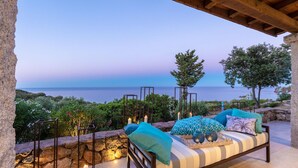 A cozy outdoor seating area with a view of the sea, a stone wall, and a wooden pergola. - Villa La Bella in Ottiolu (Budoni)