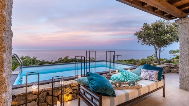 A poolside area with a view of the sea, a stone wall, and a wooden pergola. - Villa La Bella in Ottiolu (Budoni)