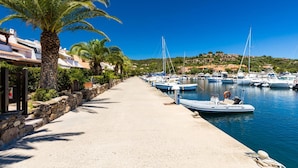 A marina with boats docked along a paved walkway lined with palm trees and stone walls. - Villa La Bella in Ottiolu (Budoni)