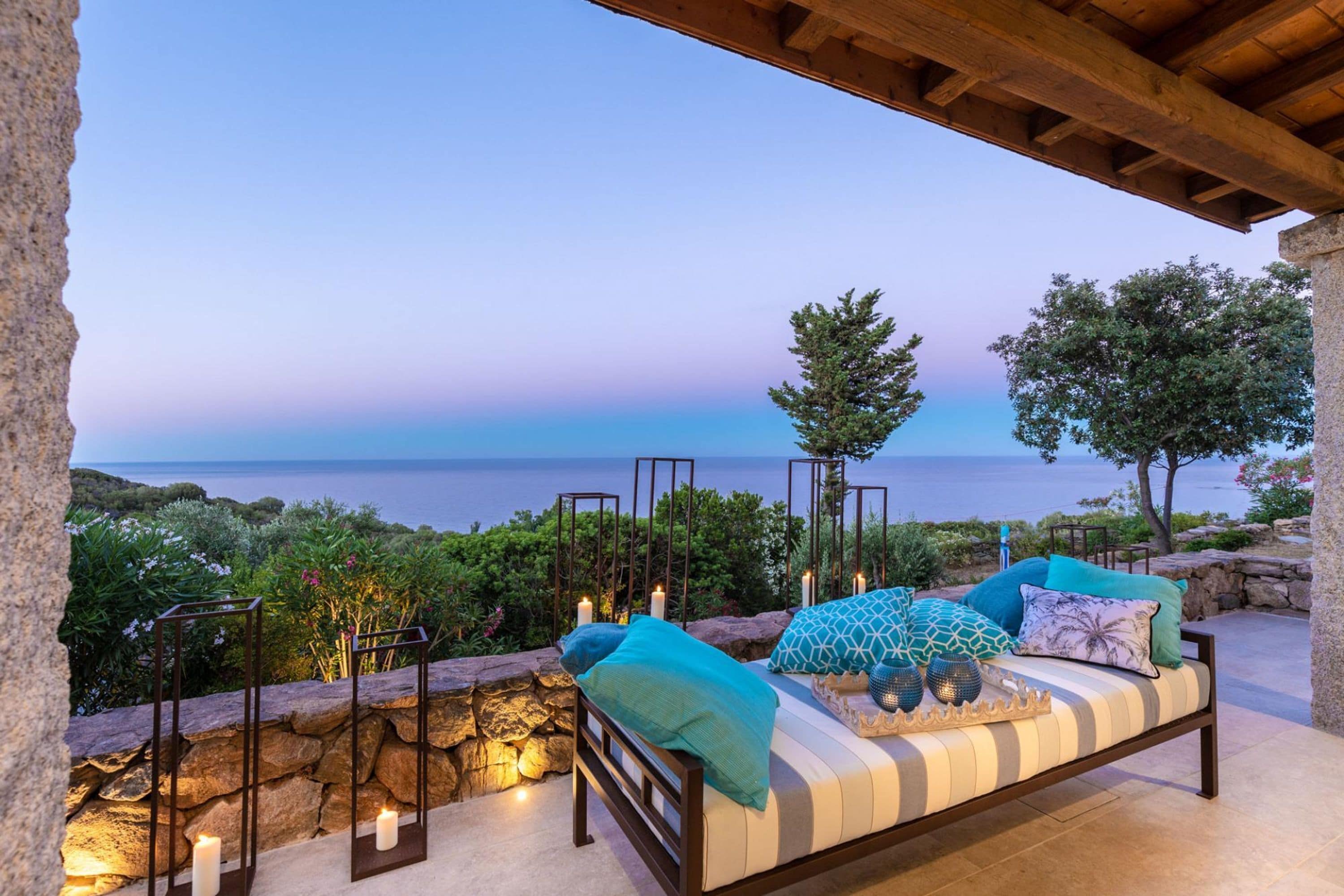 A seaside patio with a cushioned seating area, stone walls, and a view of the ocean.