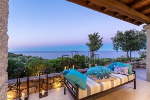 Une terrasse en bord de mer avec un coin salon agrémenté de coussins, des murs en pierre et une vue sur l’océan.