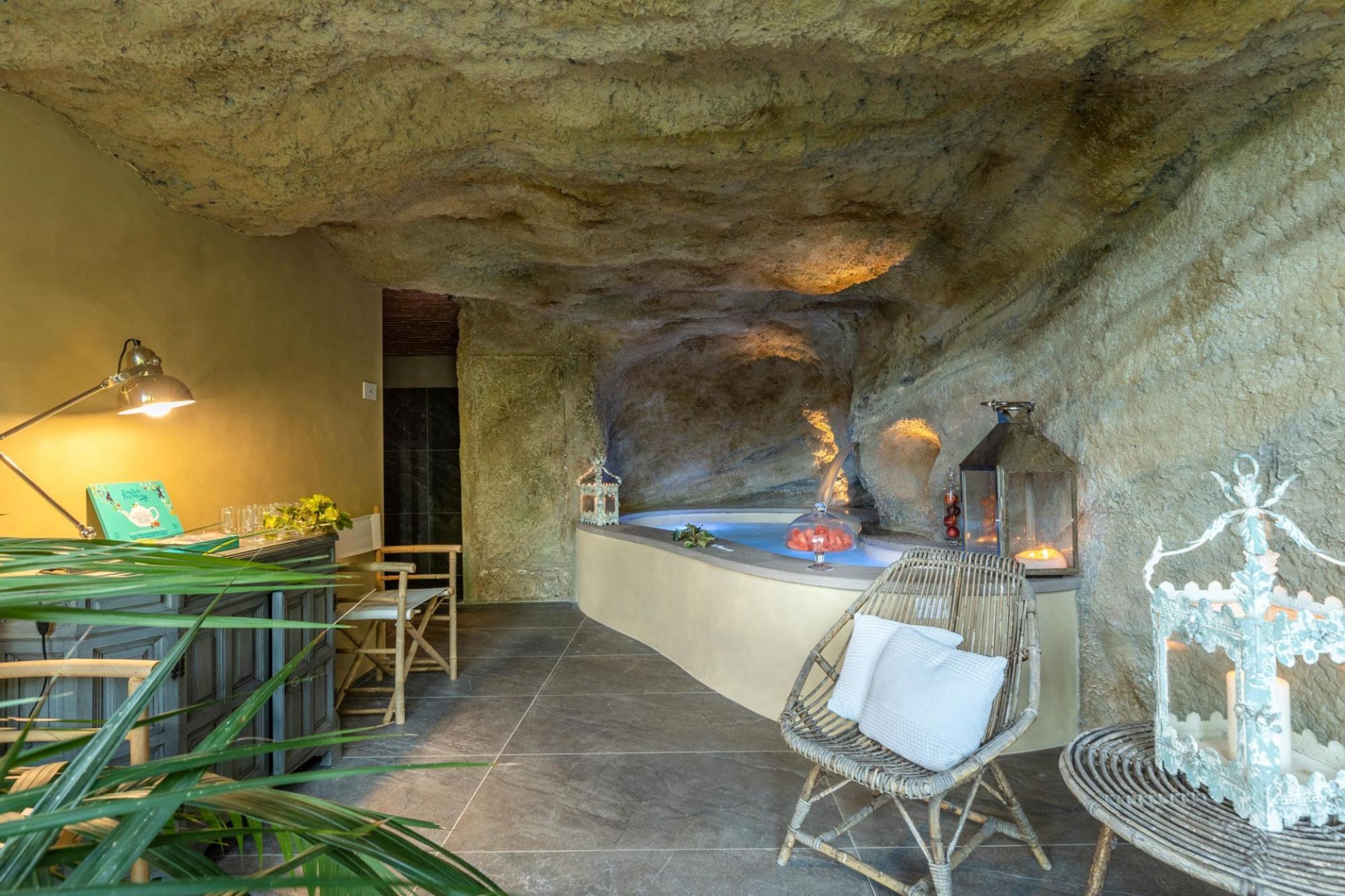 A cozy interior with a stone wall, a bar area with a drink, wicker chairs, and a lantern.