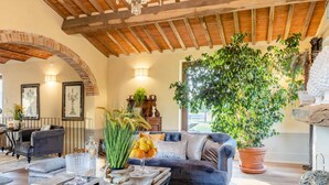 A spacious living room with a large sofa, a coffee table, and a potted plant. There is a fireplace and a chandelier on the ceiling. - Il Conte Farmhouse Retreat (Castelfranco di Sotto)