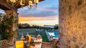 An outdoor dining area with a view of a swimming pool, stone walls, and wicker furniture. - Il Conte Farmhouse Retreat (Castelfranco di Sotto)