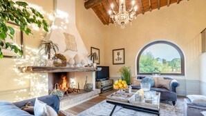 A cozy living room with a fireplace, comfortable seating, and a large window offering a view of greenery. - Il Conte Farmhouse Retreat (Castelfranco di Sotto)