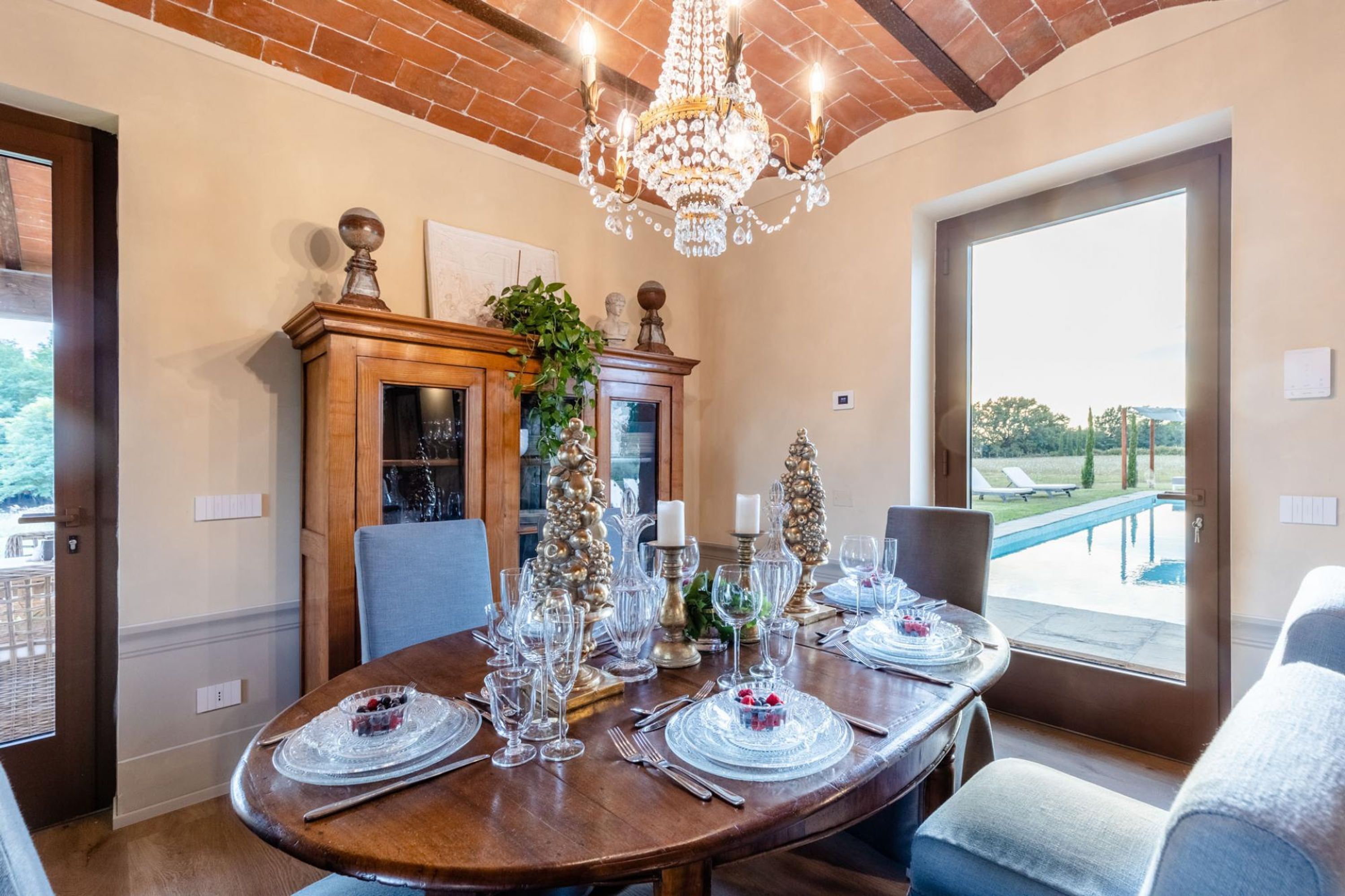 A dining room with a wooden table set for a meal, a chandelier, and a view of a swimming pool.