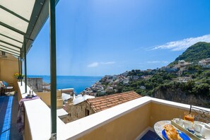 A balcony with a view of a coastal town, a table with breakfast items, and a clear blue sky. - Amore Rentals - Casa Barbera A (Positano)