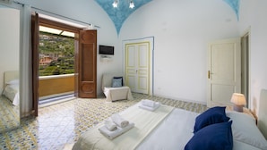 A bedroom with a bed, a chair, a TV, and a door. - Amore Rentals - Casa Barbera A (Positano)