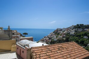 A coastal town with terracotta-roofed buildings, a clear blue sky, and a view of the sea. - Amore Rentals - Casa Barbera A (Positano)