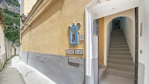 A narrow street with a building featuring a staircase and signs indicating room names. - Amore Rentals - Casa Barbera A (Positano)