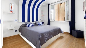 Egy modern hálószoba, ívelt mennyezettel, nagy ággyal, csíkos párnákkal, éjjeliszemmel és függönnyel ellátott ablakkal.