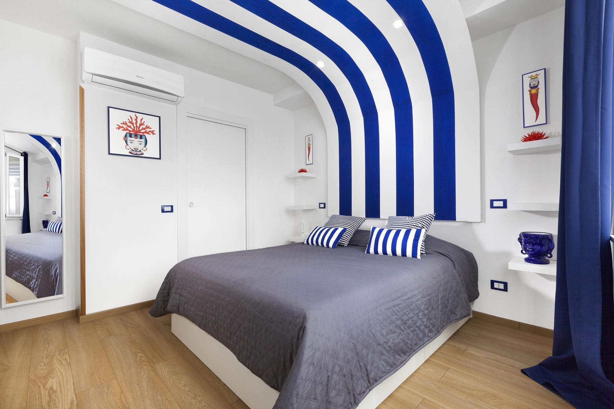 A bedroom with a bed, a mirror, and a blue and white striped wall design.