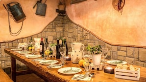 Een lange eettafel gedekt met borden, glazen en flessen, omgeven door stenen muren en rustieke decoratie.