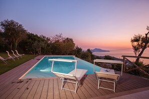 A swimming pool with lounge chairs and a deck overlooking a scenic view.
