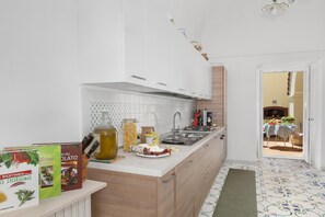 Une cuisine moderne avec des meubles blancs, un îlot central et un coin repas visible à travers une porte ouverte.