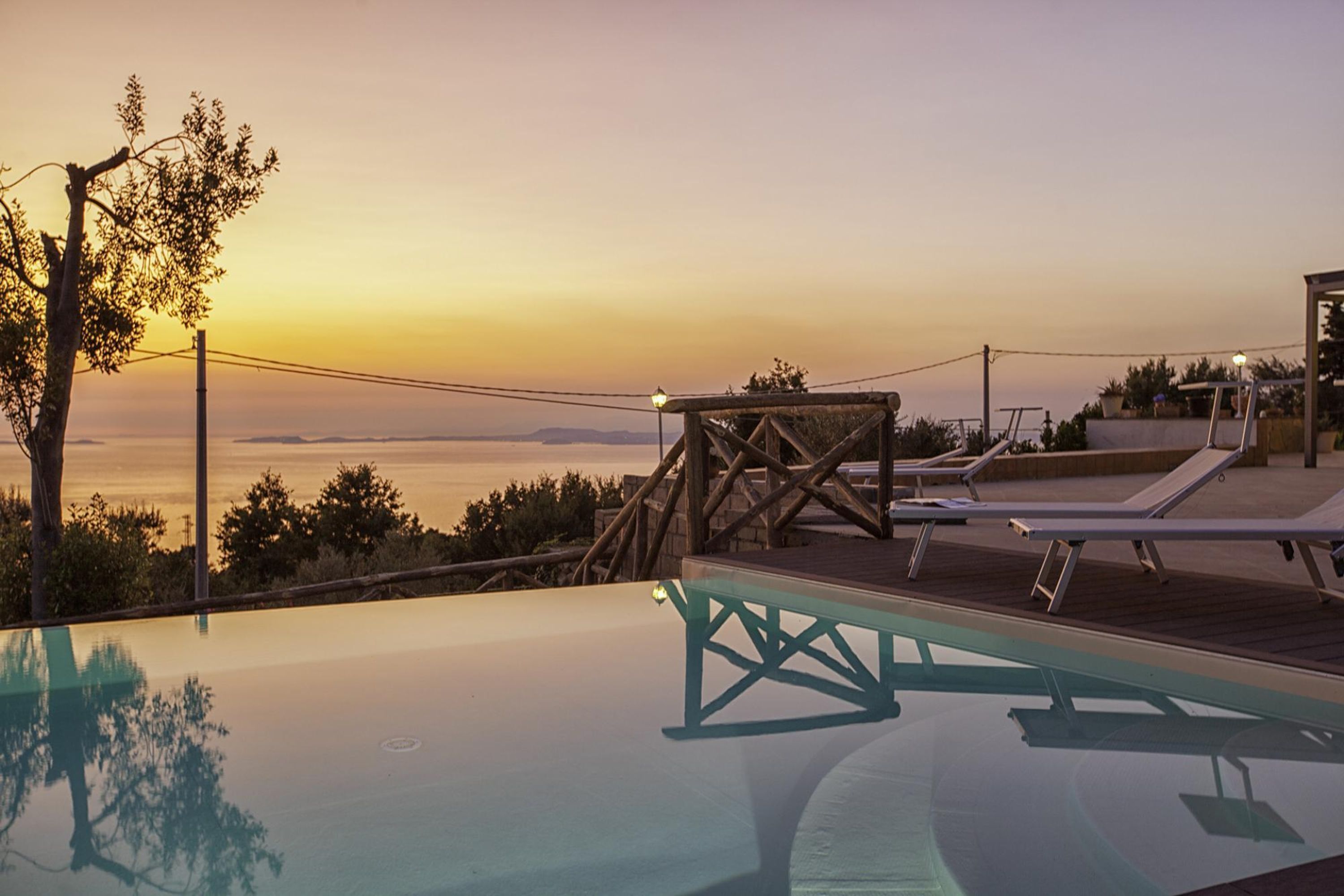 A clear view of a swimming pool with a sunset in the background, a wooden deck, and lounge chairs.