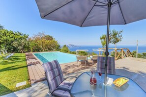 Un espace aménagé au bord de la piscine, avec une table en verre, des coussins à rayures et une vue sur la mer.