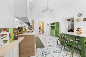 Une cuisine moderne avec un coin repas, comprenant un plan de travail en marbre, des chaises vertes et un lustre.