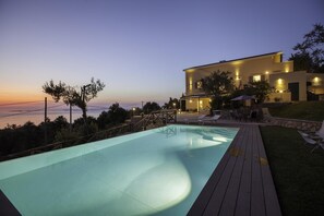 A modern house with a swimming pool, outdoor furniture, and a view of the sea.