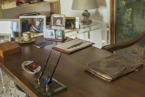 A wooden desk with a glass top, a lamp, a mug, a pen holder, a notebook, and a book.