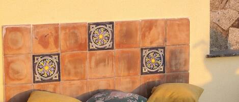 A tiled bench with decorative tiles and cushions against a wall.