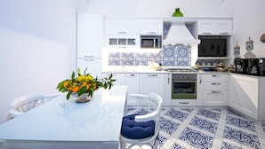 A modern kitchen with white cabinets, a blue and white patterned backsplash, and a dining area with a glass table and blue cushioned chairs. - Maison Don Rafe in Positano (Positano)