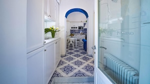 A narrow hallway with white cabinets and a blue-tiled floor leading to a kitchen area with white cabinets and a blue archway. - Maison Don Rafe in Positano (Positano)