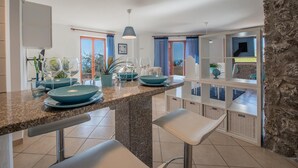 Een moderne keuken met granieten aanrecht, blauwe borden en witte barkrukken.