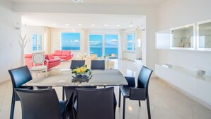 A modern dining area with a large table, black chairs, and a chandelier. There is a red sofa and a white chair in the background, with a view of the sea through large windows. - Villa Ado in Sorrento (Sorrento)