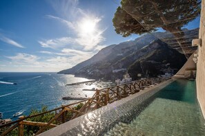 Hotel à beira-mar com piscina e vista para o oceano, deck de madeira e paisagem montanhosa ao fundo.