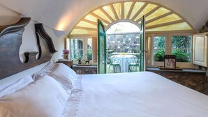 A bedroom with a large bed, a stone wall, and a view of an outdoor dining area. - Villa Alma in Massa Lubrense (Massa Lubrense)