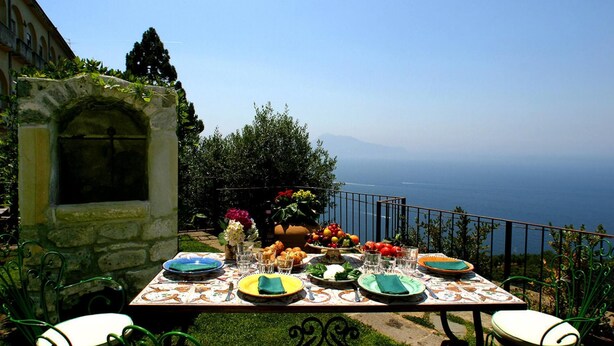 An outdoor dining table set with plates, glasses, and a fruit bowl, overlooking a scenic view of the sea. - Villa Alma in Massa Lubrense (Massa Lubrense)