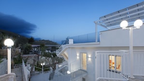A modern building with a glass facade, outdoor seating area, and a staircase leading to a balcony. - Villa Iside in Nerano (Massa Lubrense)