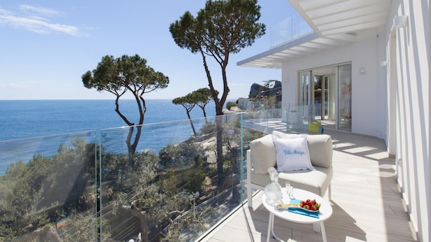 A balcony with a clear view of the sea, white furniture, and a glass railing. - Villa Iside in Nerano (Massa Lubrense)