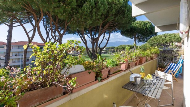 A balcony with potted plants, a table with glasses, and a view of the sea and buildings. - La Casa Matta in Viareggio (Viareggio)