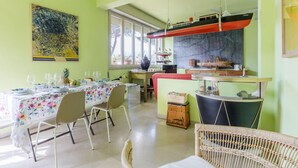 A dining area with a table set for a meal, chairs, a decorative wall, and a kitchen area with a stove and a hanging boat model. - La Casa Matta in Viareggio (Viareggio)