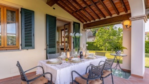 An outdoor dining area with a table set for four, surrounded by chairs with cushions. - Nonna Bianca Farmhouse (Lucca)