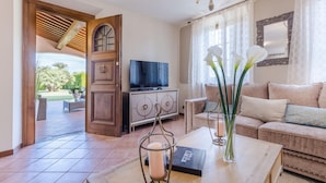 A living room with a TV, sofa, coffee table, and a view of the outdoors. - Nonna Bianca Farmhouse (Lucca)