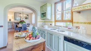 A kitchen with a central island, a dining area with a chandelier, and a view of the outside through a window. - Nonna Bianca Farmhouse (Lucca)